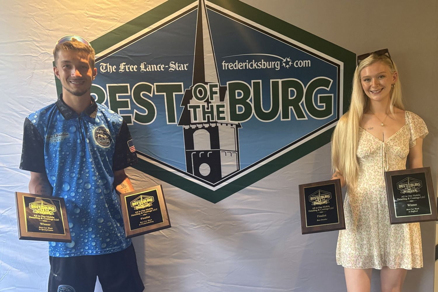 The All-In-One owner and his spouse holding four Best of the Burg 2025 plaques in front of the Best of the Burg backdrop